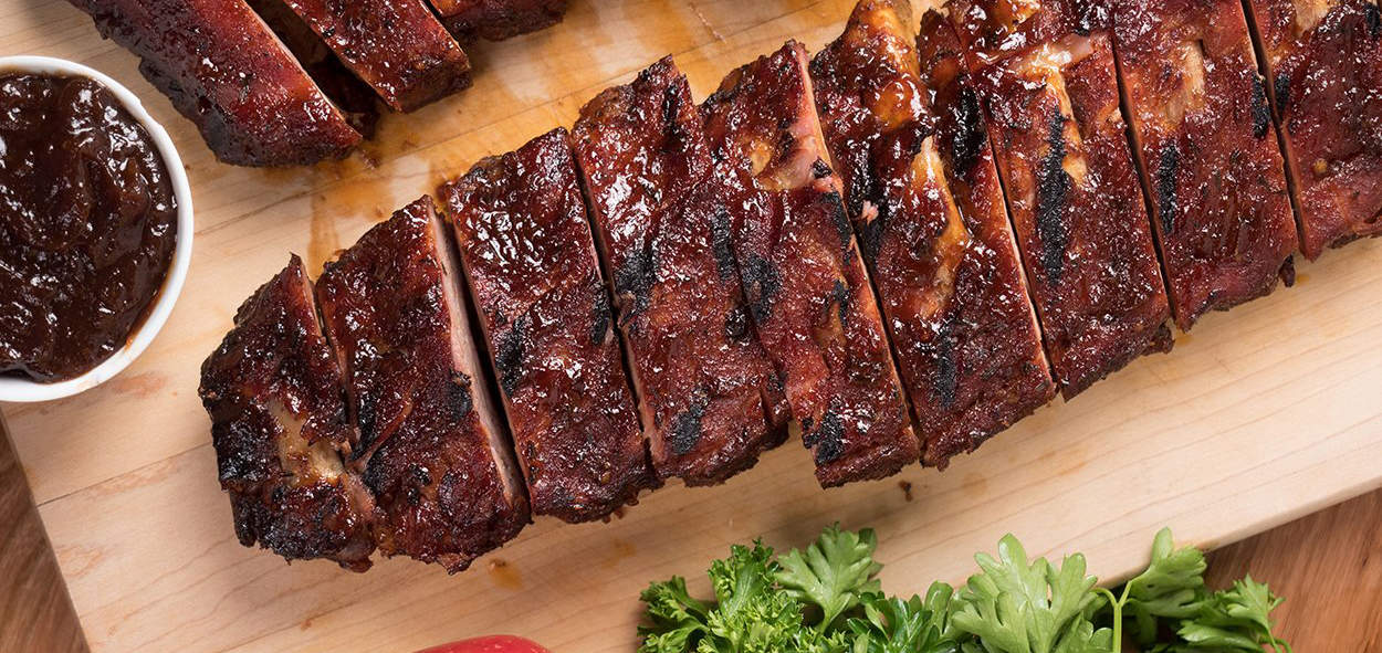 Succulent barbecued ribs with smoky glaze and side of sweet sauce on wooden platter.