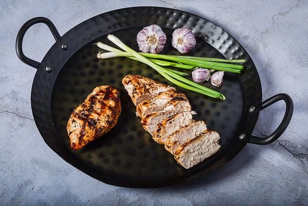 Grilled chicken breast with fresh green onions and garlic on a black grill pan.