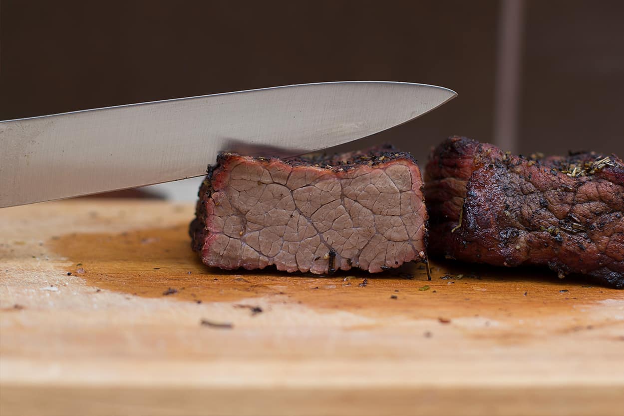 Juicy, perfectly cooked beef steak cut on a wooden board with a kitchen knife.