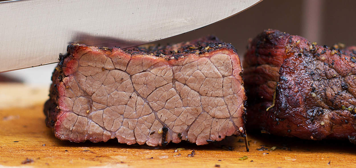 Juicy, perfectly cooked beef brisket sliced on a wooden cutting board for BBQ and smoking.