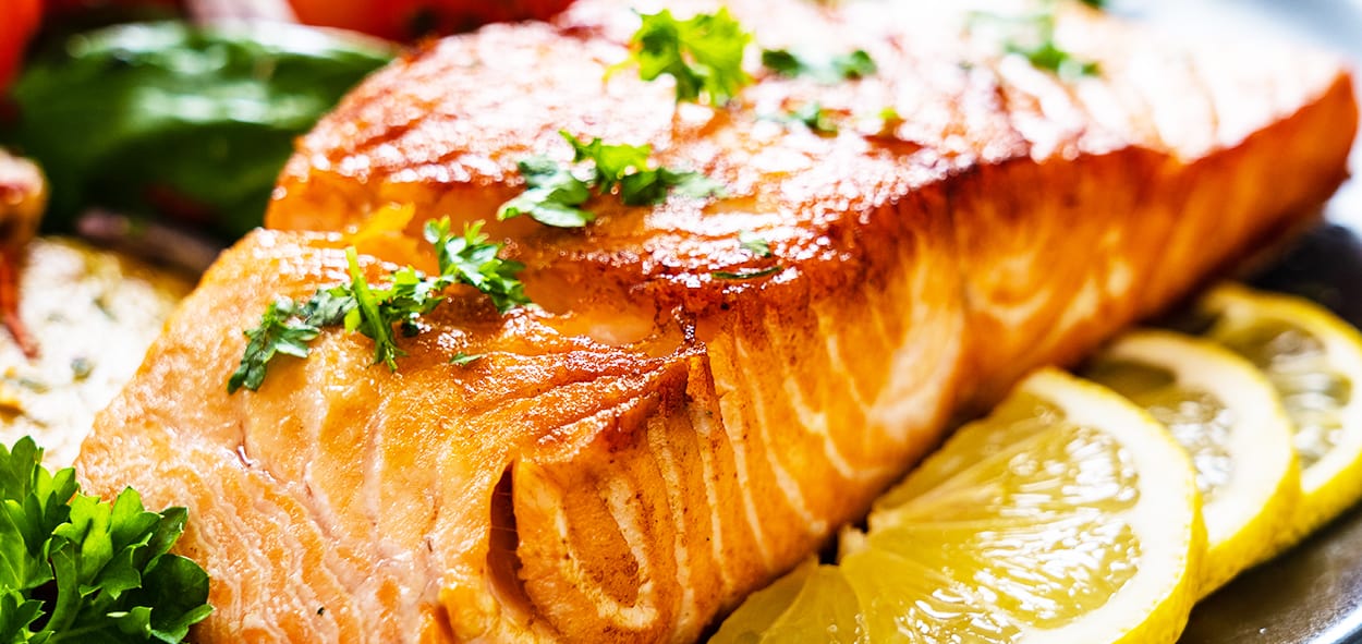 Freshly cooked salmon fillet garnished with herbs and lemon slices for healthy eating.