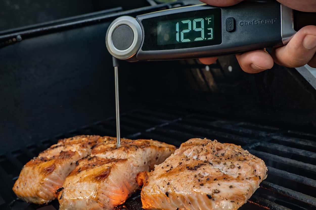 Digital meat thermometer displaying 129.3°F, measuring cooked chicken on grill.