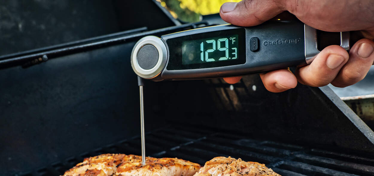 Digital meat thermometer for grilling at 129.3°F | ChefsTemp digital meat thermometer used for perfect grill results | a hand holding a ChefsTemp digital meat thermometer measuring food temperature on a grill.