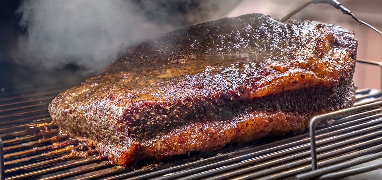 Juicy smoked brisket cooking on a grill with smoke rising for delicious barbecue flavor.
