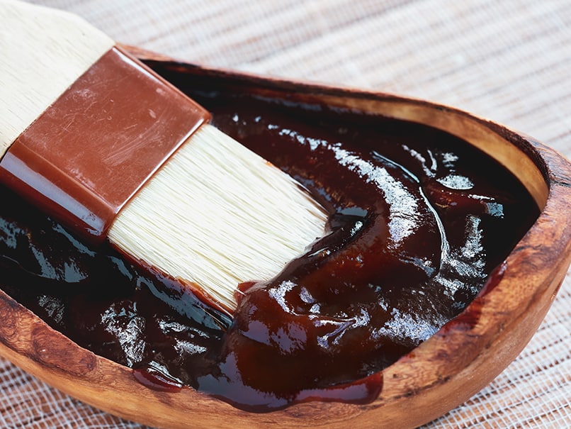 Dark soy sauce being brushed onto a dish in a wooden bowl with a basting brush, highlighting cooking techniques and Asian cuisine.