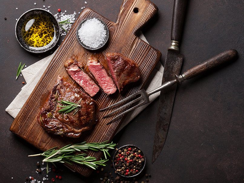 Juicy, perfectly cooked steak on wooden cutting board with seasoning and herbs.