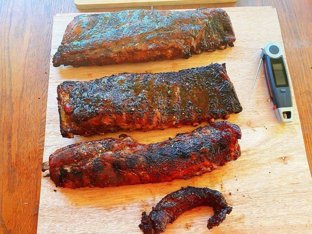 Succulent smoked ribs with a digital thermometer on a wooden cutting board.