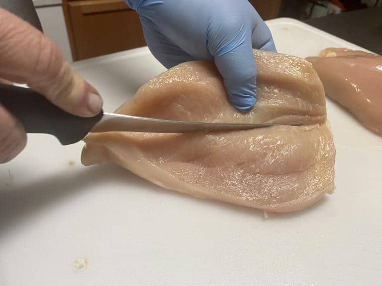 Fresh chicken breast being precisely cut with a chef's knife for food prep safety and quality.