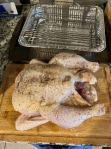 Raw whole chicken seasoned with spices on a wooden cutting board with a cooling rack in background.