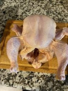 Raw whole chicken on cutting board ready for cooking.