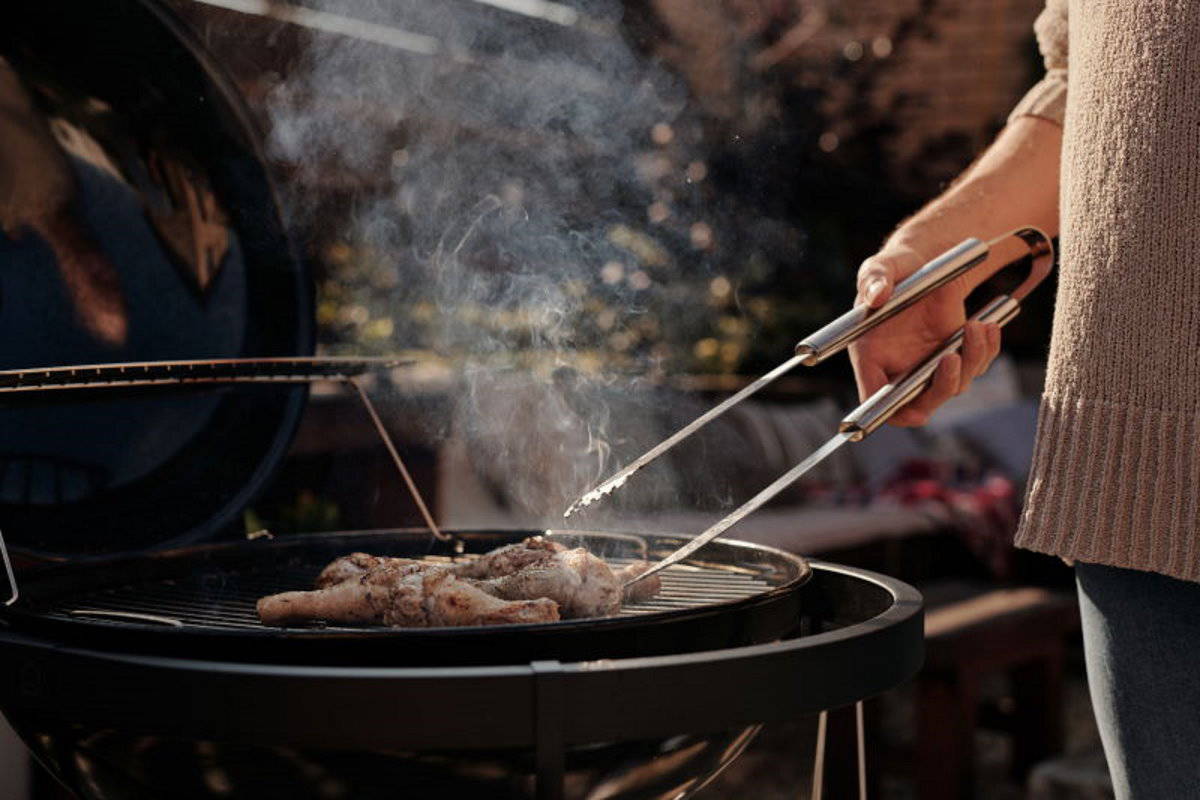 Grilling meat outdoors with stainless steel tongs for perfect barbecue cooking.