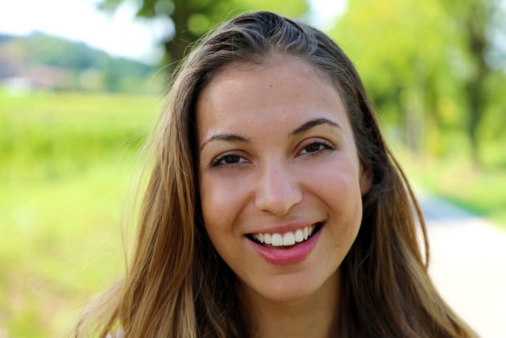 Close-up of a smiling young woman outdoors with bright, natural background.