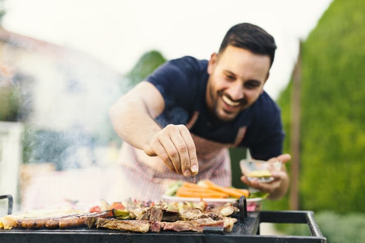 Seasoned man grilling steak and vegetables outdoors on barbecue grill.