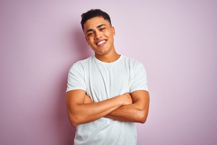 Smiling young man standing confidently against pastel pink background.
