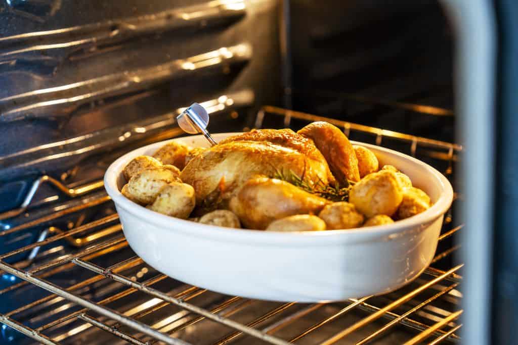 Roasted whole chicken with potatoes baking in an oven, flavorful and perfectly cooked.