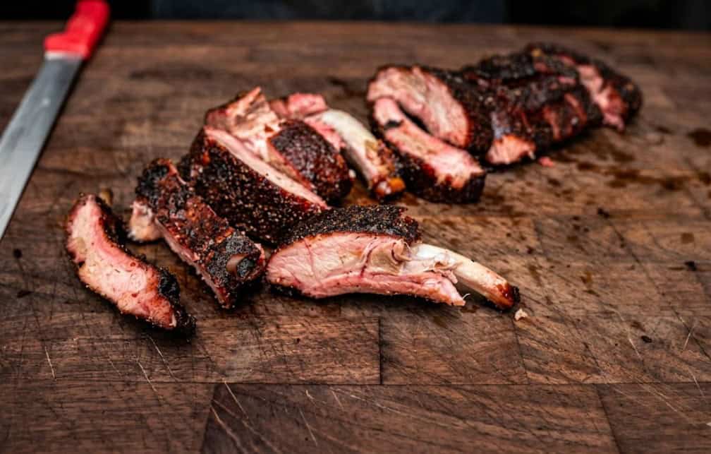 Juicy, smoked ribs sliced on a wooden cutting board, showcasing perfect grilling results.
